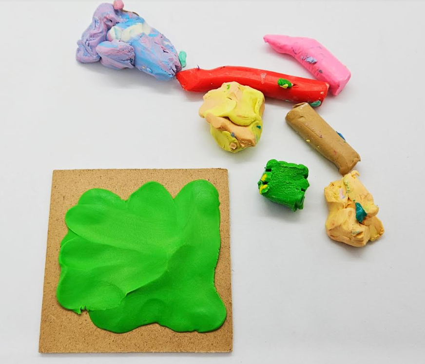 spring craft for kindergarten shows a bunch of plasticine and a wooden square with green clay smeared on it.