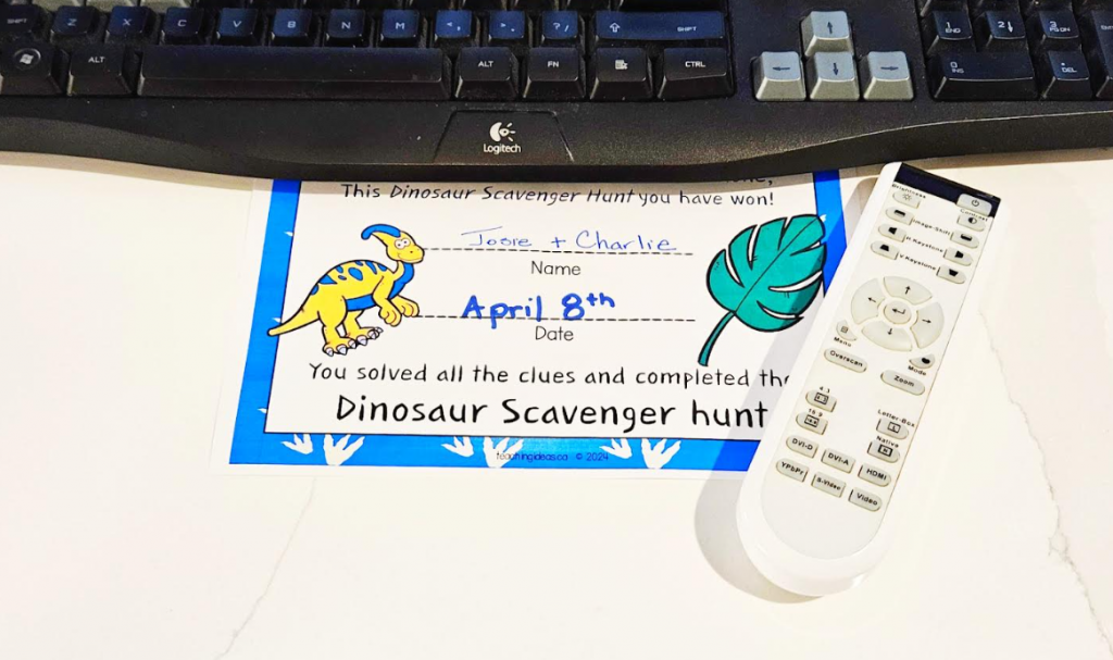free dinosaur scavenger hunt shows a printed clue set beside a computer keyboard and controller.
