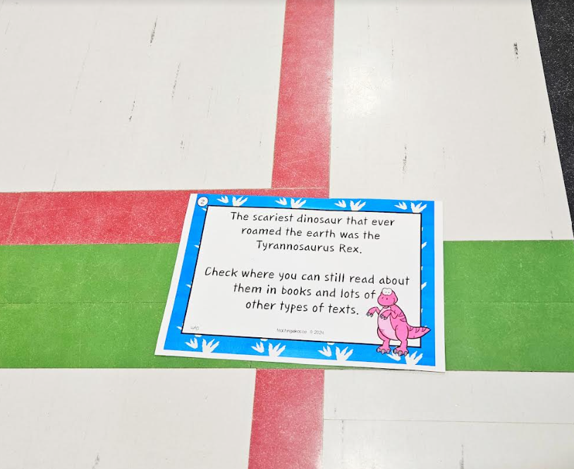 free dinosaur scavenger hunt shows a printed riddle placed on a gym floor.