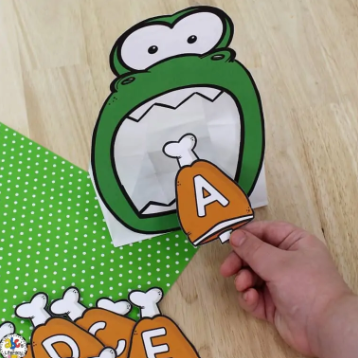 dinosaur learning activity shows a dinosaur clipart with its mouth open and a child putting a letter A clipart card into the mouth.
