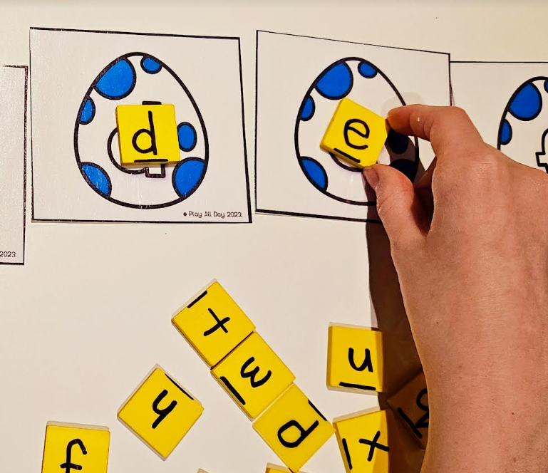 dinosaur activities for kids shows a child putting a letter E block onto a matching egg card.