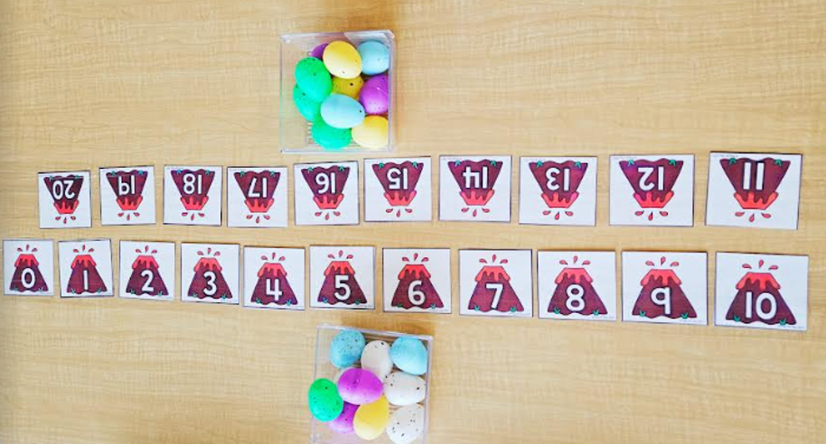 dinosaur activities for kids shows two rows of numbers printed with a volcano background and two bins of eggs.