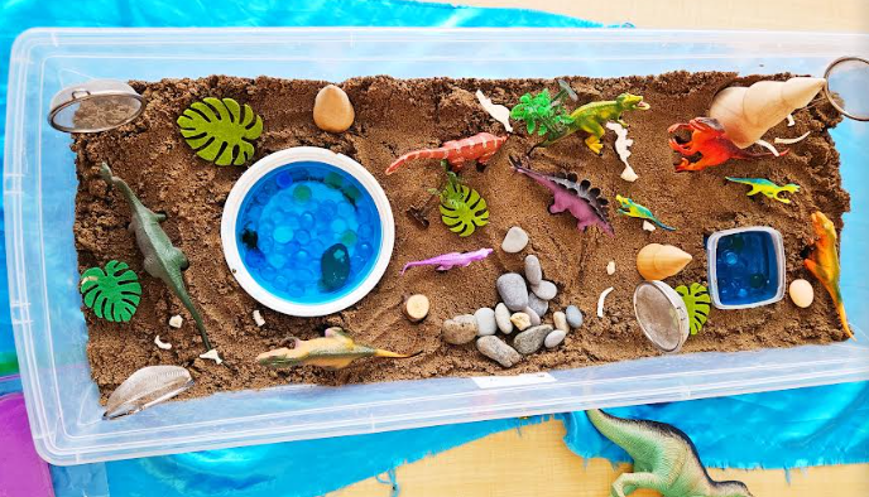 sensory play for kids shows a bin filled with sand and dinosaur materials.
