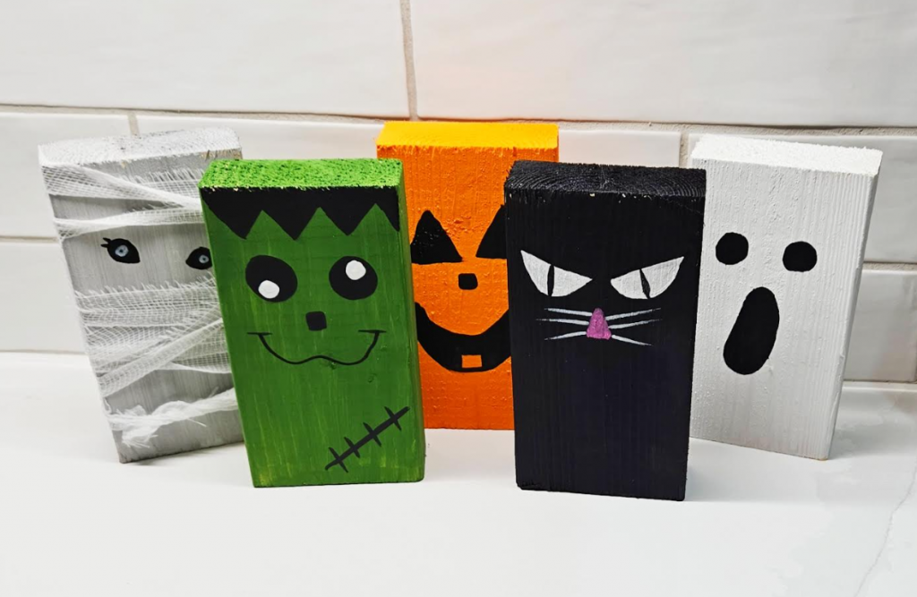 easy halloween craft for kids shows five wooden blocks painted Halloween themed, a ghost, mummy, Frankenstein, cat, pumpkin.