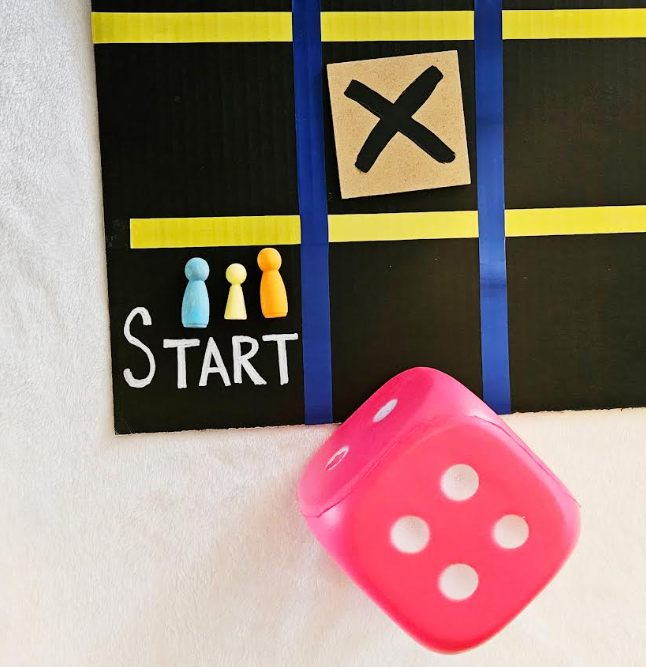 DIY number game for kids shows the bottom of a board game that says START and has a pink dice, wooden people and a wooden square X.