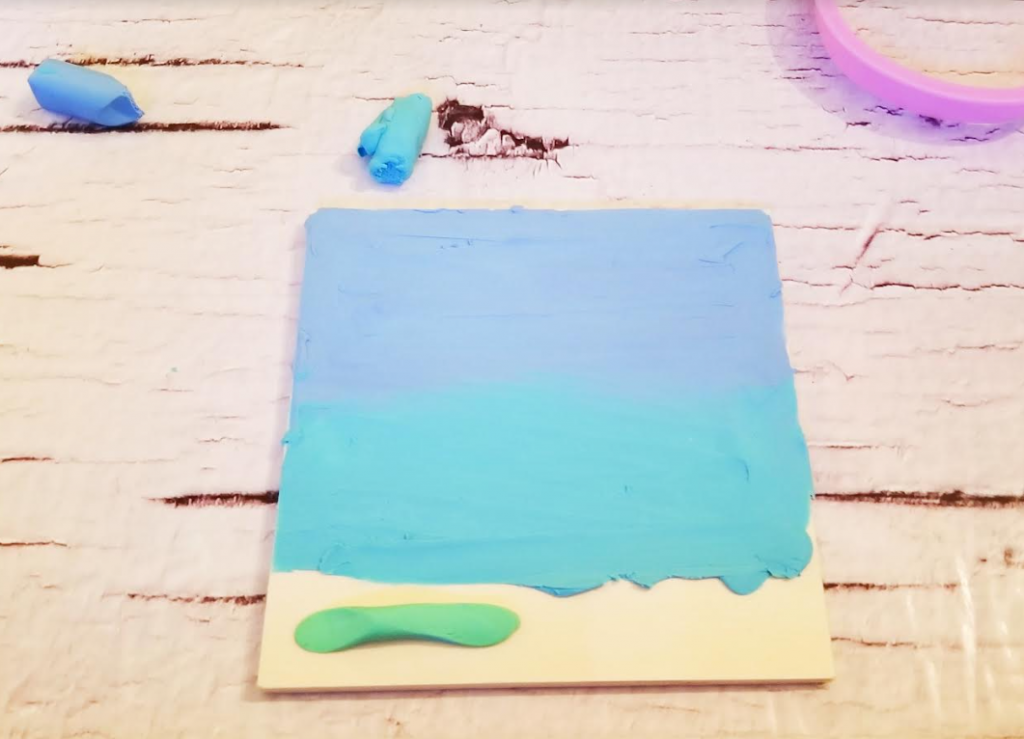spring craft for kindergarten shows a wooden square with a gradient of blue plasticine on it.