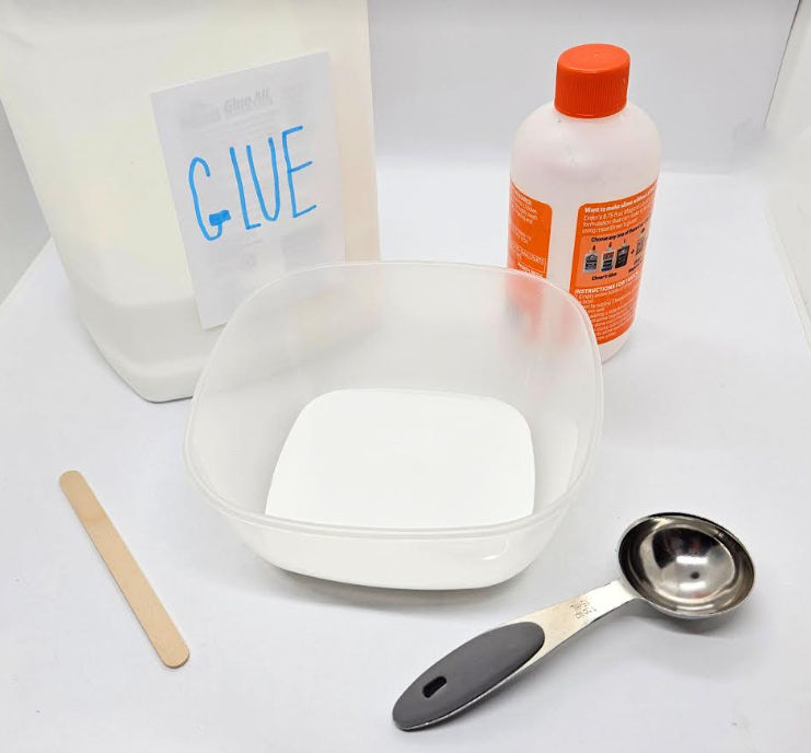 sensory play shows a bottle of glue, slime activator container, bowl of glue, popsicle stick and measuring spoon.