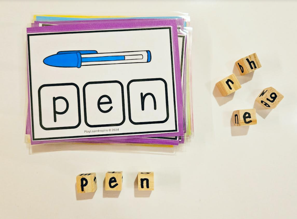 word family game shows a stack of cards and the top one says pen and small wooden cubes with letters on each.