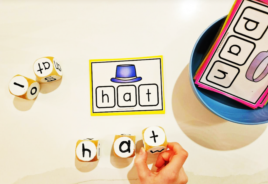 phonics for kindergarten shows a child putting together the word HAT and a word card and bowl of word family cards.