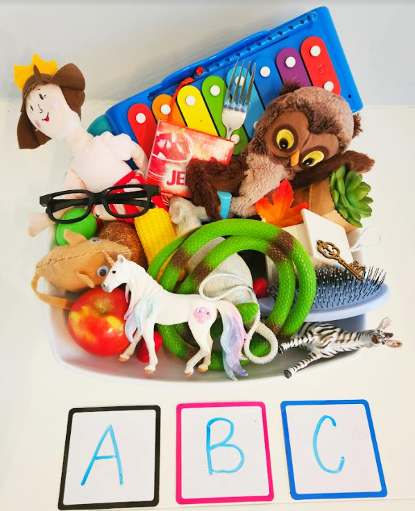 alphabet activity for kindergarten and preschool shows a bin with a bunch of objects in the bin and the letters ABC printed on boards below the bin.