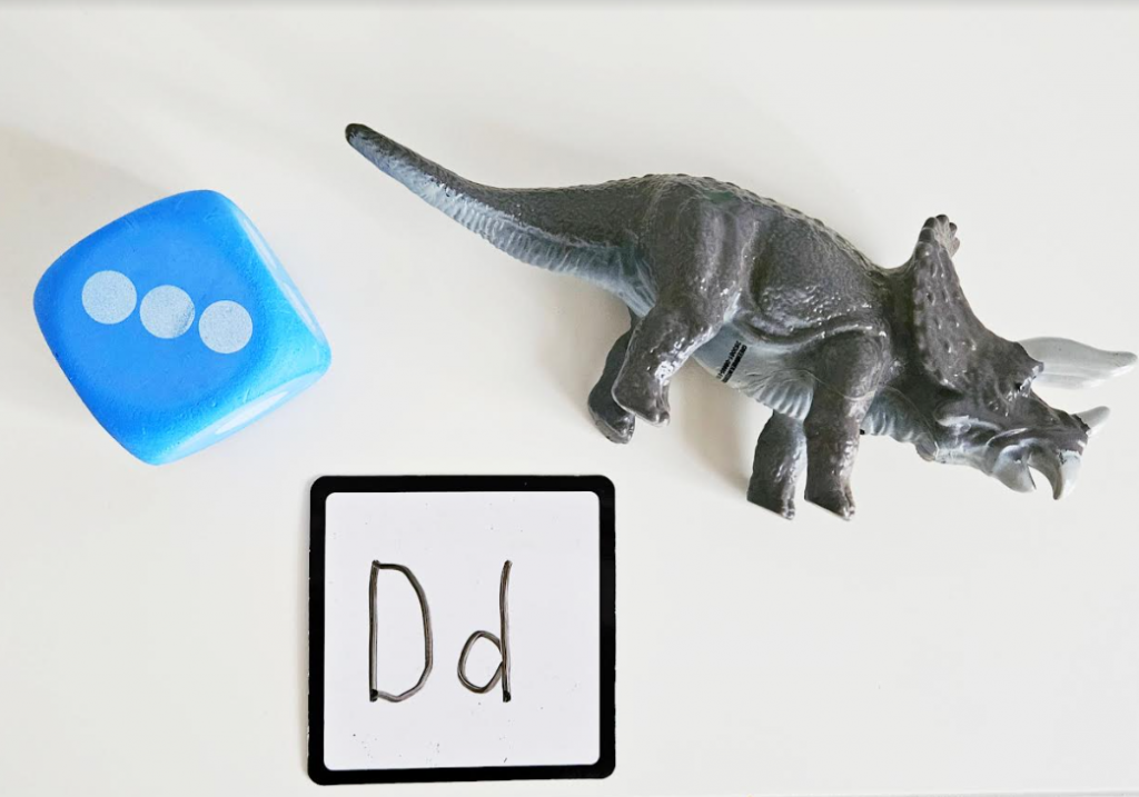 alphabet activity for kindergarten shows a dinosaur and dic and a board with the letter Dd printed below it.