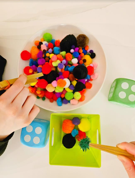 Easy Kindergarten Math Activity shows children putting pompoms in a container with two dice in the corner.