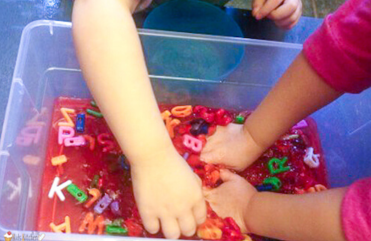 sensory alphabet activity shows kids playing in jello that has plastic letters throughout.