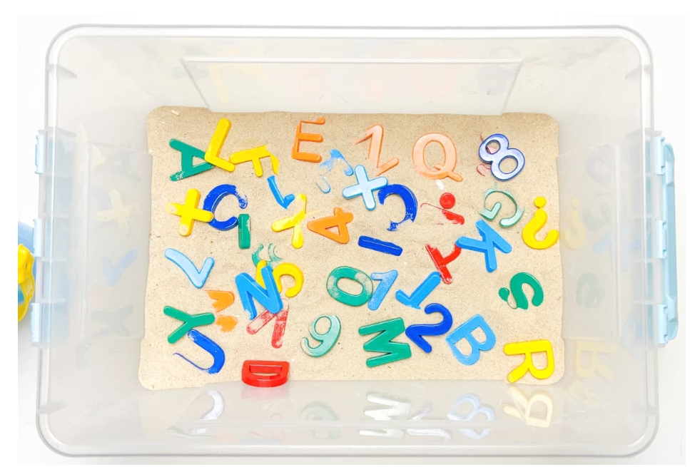 easy alphabet sensory bin shows a bin filled with sand and letters.