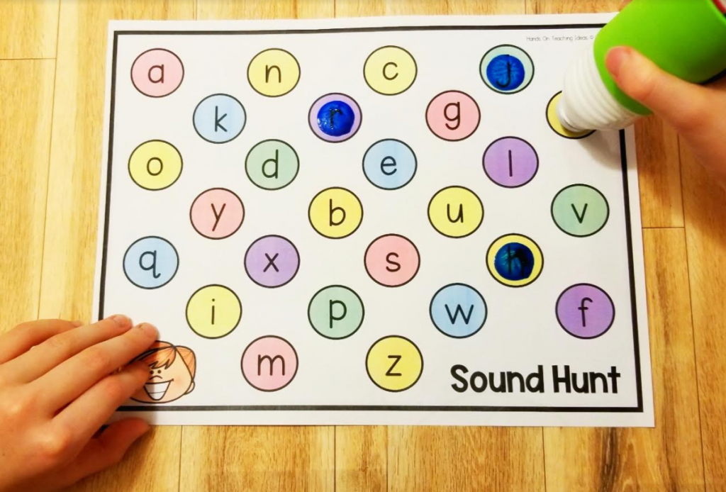 phonics activity shows a child using a bingo dabber and dabbing letters on an alphabet page.