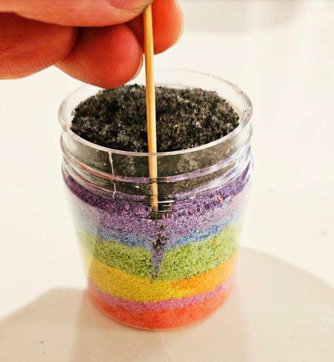 easy summer craft for kindergarten shows layers of chalk salt in a jar and a toothpick being pushed down the side.