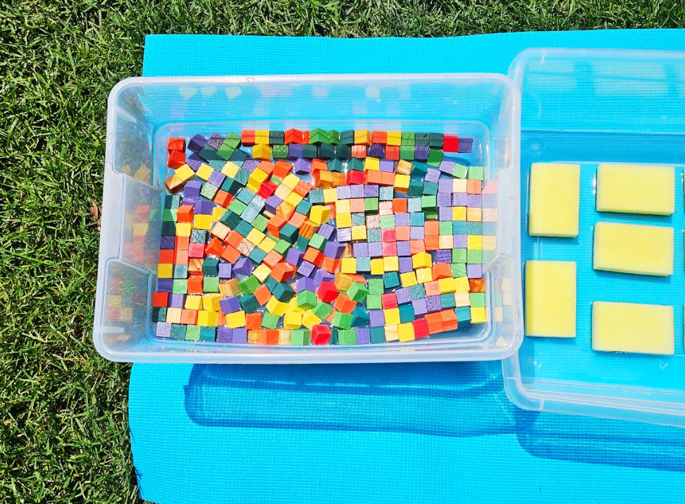 summer sensory walk shows a bin with colorful wooden cubes.