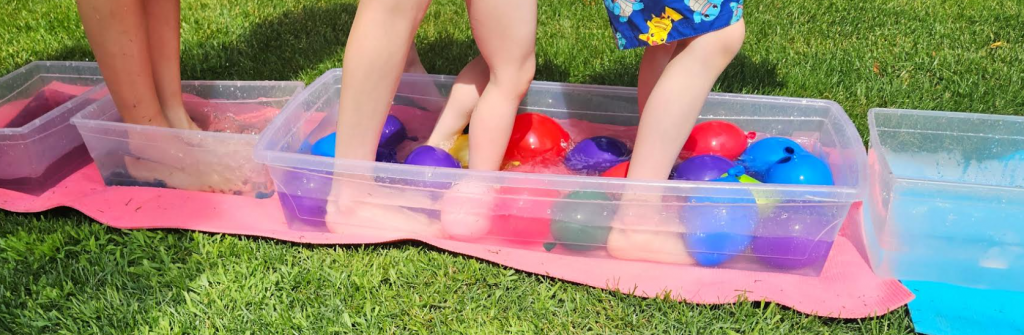 outdoor learning activity shows children walking through bins with water balloons.
