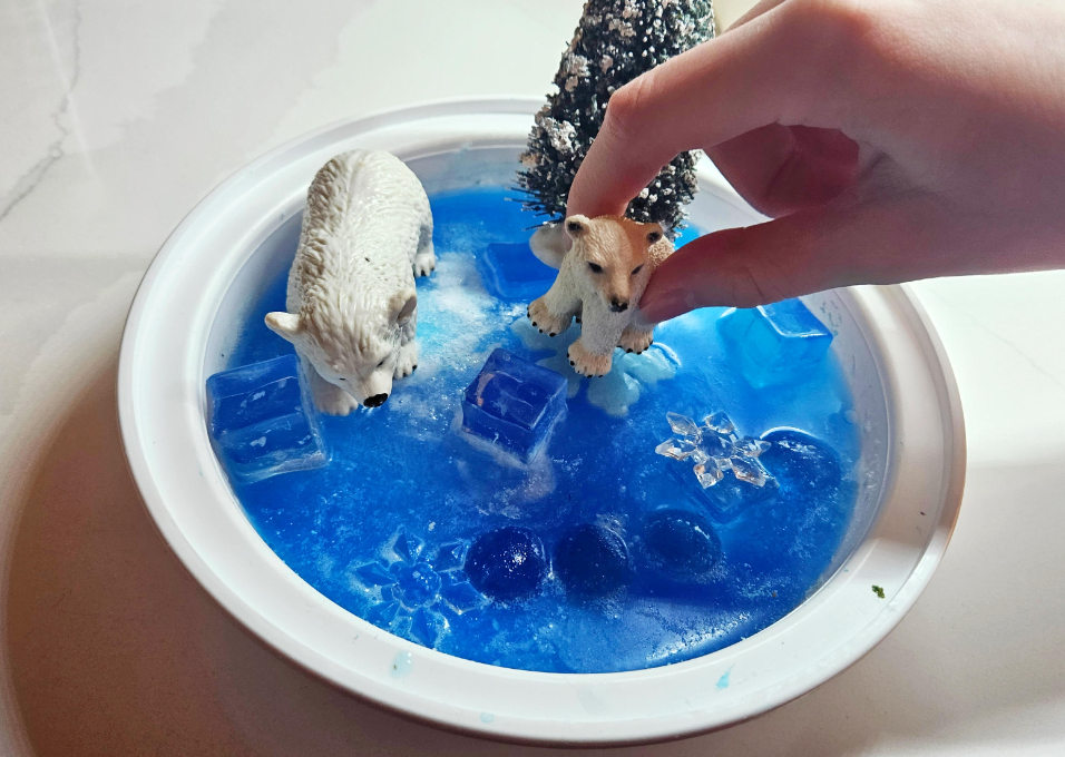small world play shows a child playing with a polar bear figure in a small tray of frozen blue water.