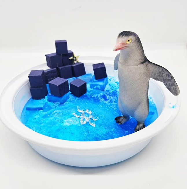preschool winter activity shows a penguin in a small tray of frozen water.