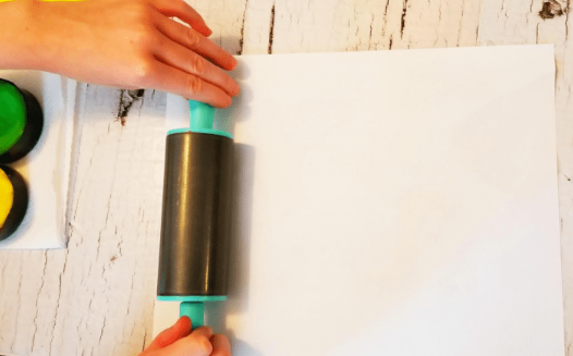 art for kids shows a child pressing cardstock paper down with a rolling pin.
